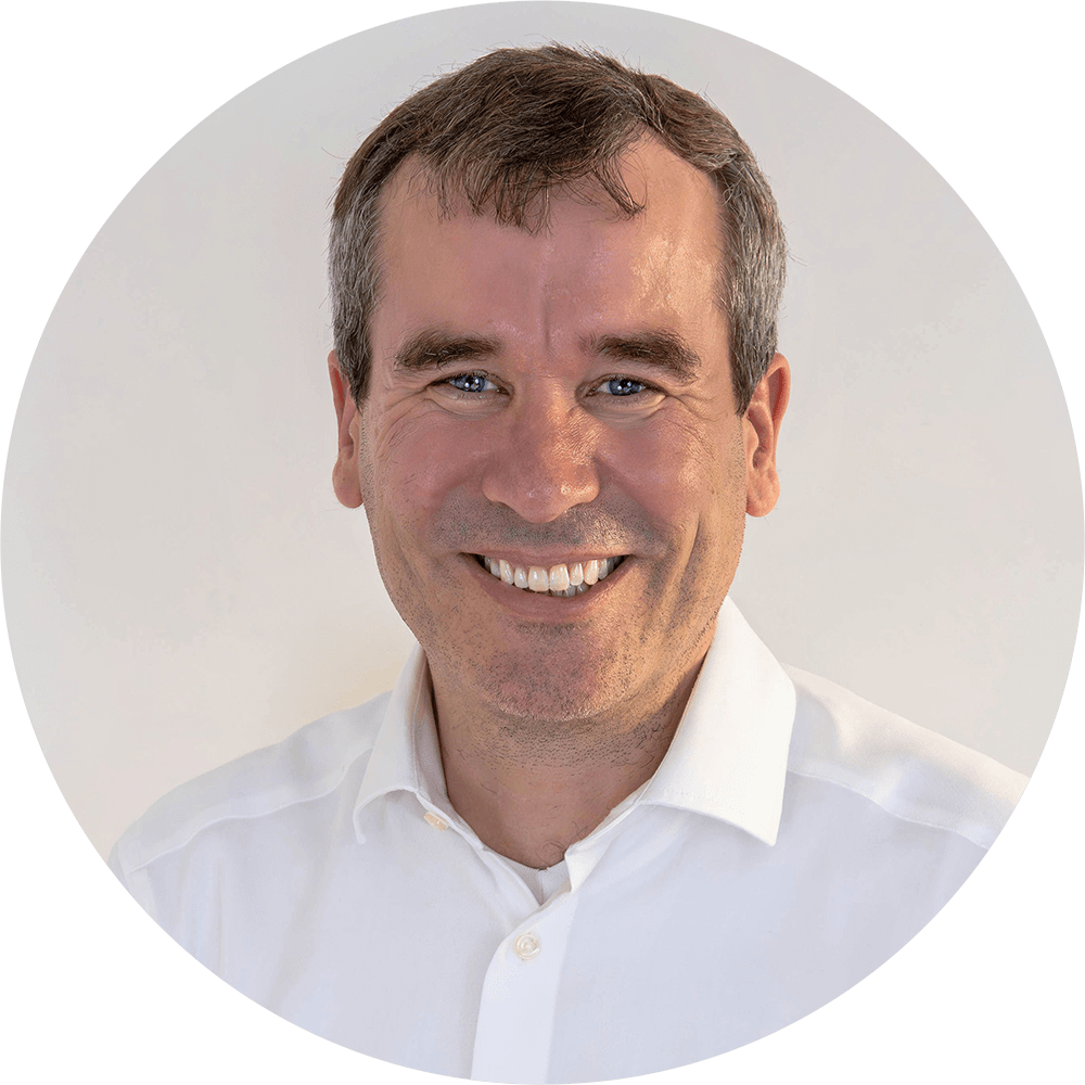 Porträt von Alexander Brendecke im weißen Hemd vor hellem Hintergrund.