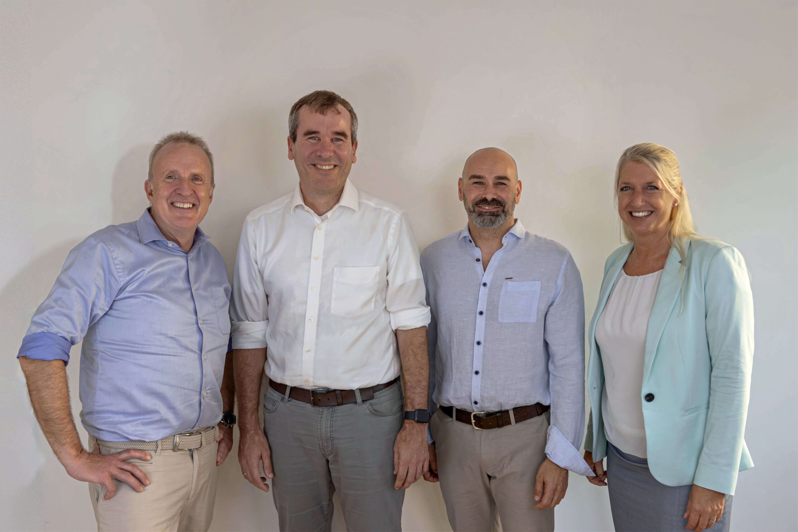 Gruppenfoto von vier Personen im Business-Outfit, darunter Alexander Brendecke in weißem Hemd, vor neutralem Hintergrund.
